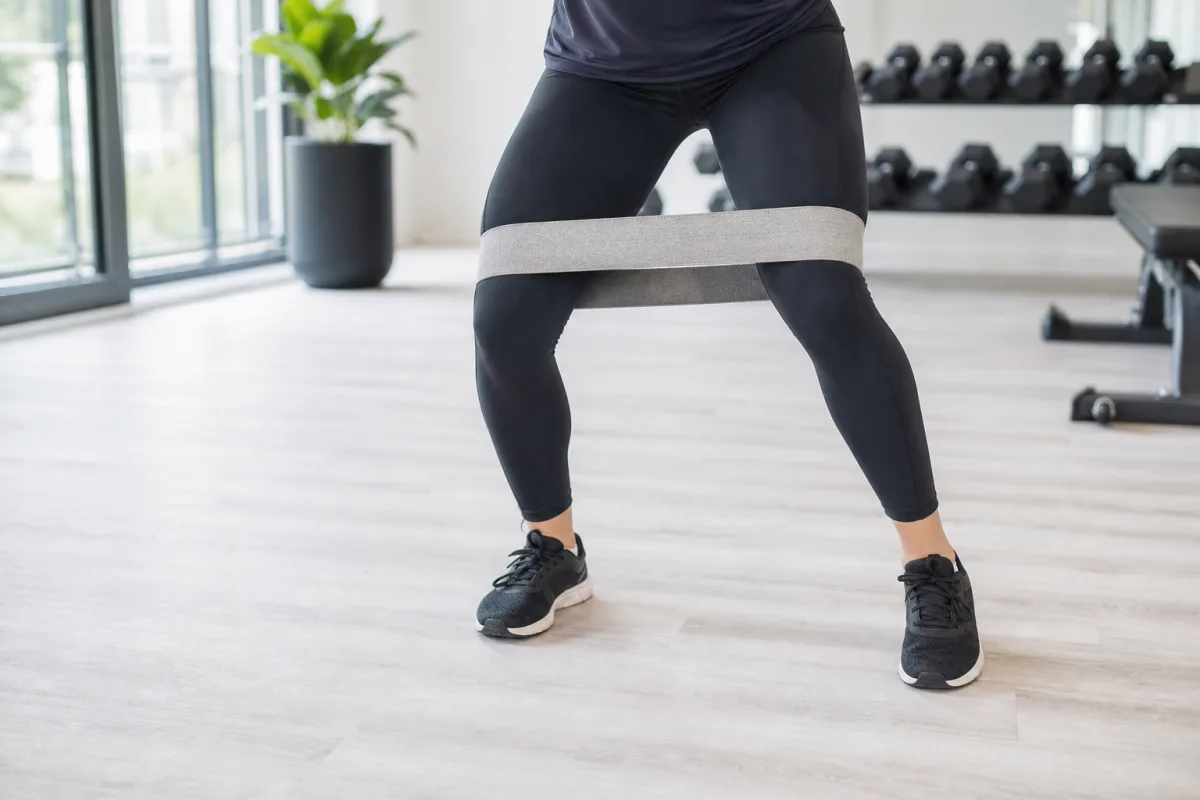 A person's legs performing a banded lateral walk with a resistance band above the knees in a bright gym